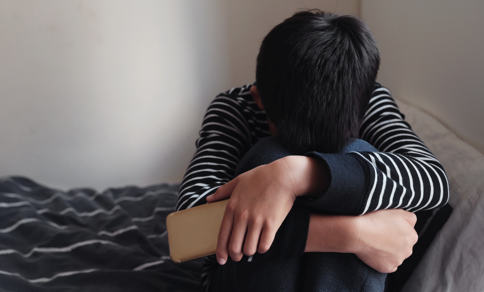 Vulnerable boy sat on bed head in knee